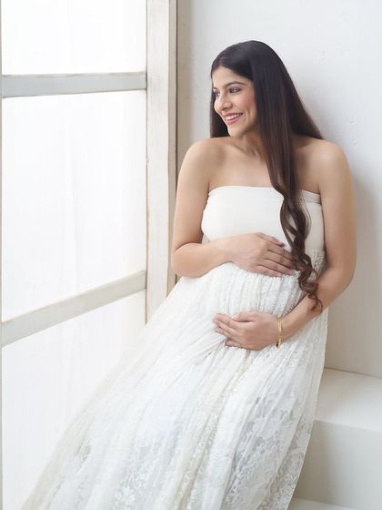 A happy, candid moment captured by the window. The mother-to-be's joyful smile and the bright, natural light make this a heartwarming and authentic portrait.