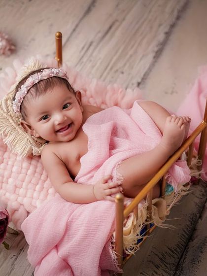 A smile that lights up the room. This older baby is so happy and expressive, nestled in her pink floral bed.