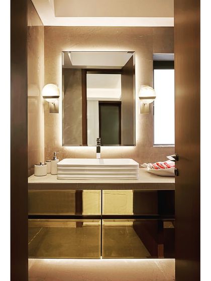 The master bathroom features a clean, modern design with a vessel sink, backlit mirror, and gold-toned cabinet fronts that add a touch of glamour.