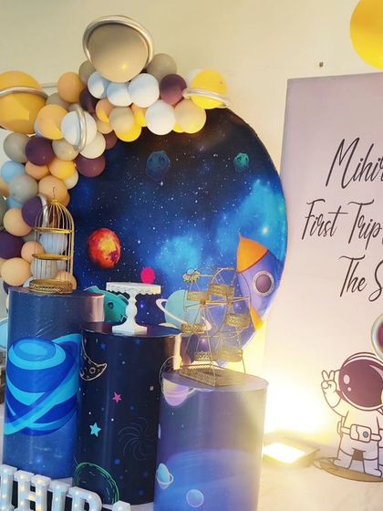 A "First Trip Around the Sun" space-themed birthday. This setup features a galaxy backdrop, astronaut cutouts, and a balloon arch with planet details.