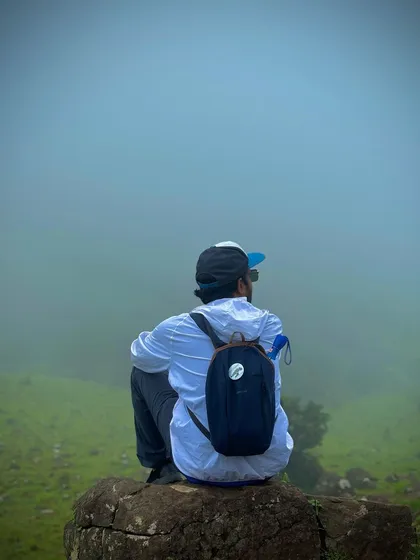 A solo traveler sitting on a rock, lost in the immense and foggy landscape of Mandalpatti in Coorg.
