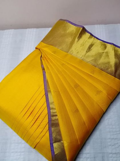 A bright yellow saree with a simple purple border. The pleats are neat and the saree is ready for a quick and easy drape.