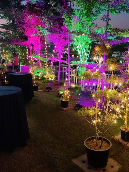 This image shows how we combine functional elements like cocktail tables with ambient lighting. The fairy lights wrapped around the trees and the colorful uplighting create a perfect party vibe.