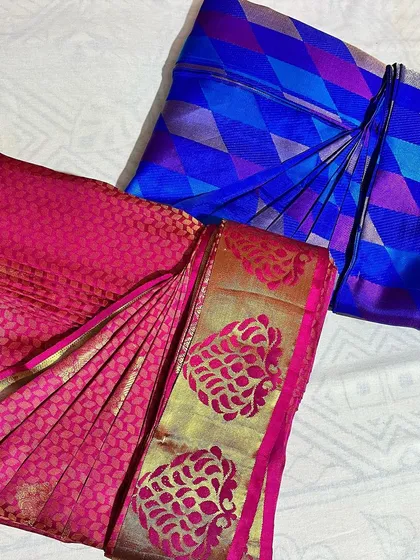A bright pink and a royal blue saree, both with intricate designs, folded to keep them in pristine condition.
