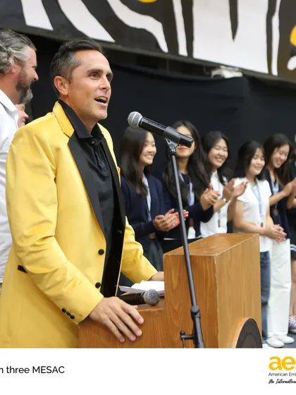 The badminton coach, in his signature yellow jacket, proudly addresses his team. Our coaches bring energy and expertise, fostering a positive and competitive environment for our athletes.
