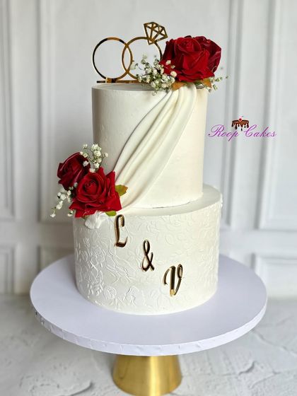 A timeless two-tier beauty for a special day. This cake is adorned with bold red roses, soft fabric-like draping, and the couple's initials in gold, celebrating romance and elegance.