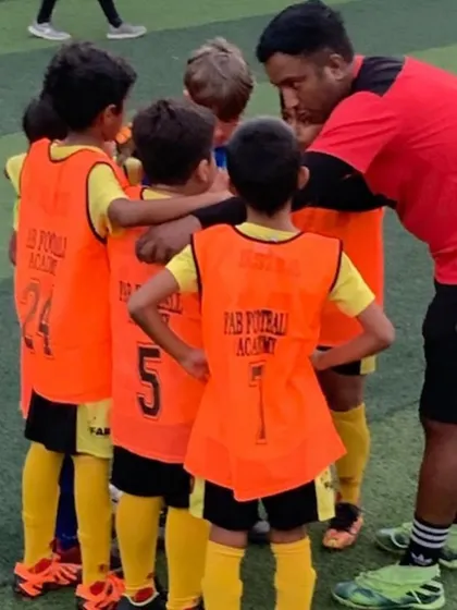 A coach in a huddle with his team. Our focus remains on nurturing young players and instilling values of teamwork and resilience.