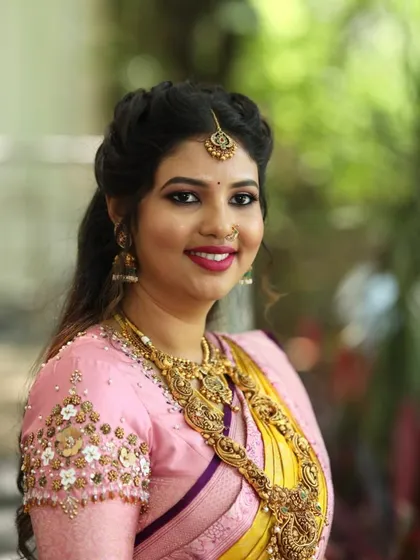 A close-up of a happy bride. Her pink blouse features delicate floral and pearl embroidery on the sleeves, adding a soft, romantic touch to her yellow and pink wedding saree.