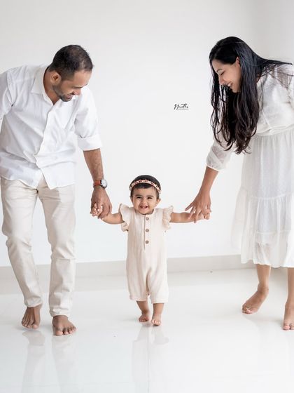 A family taking a walk together, holding their baby's hands.