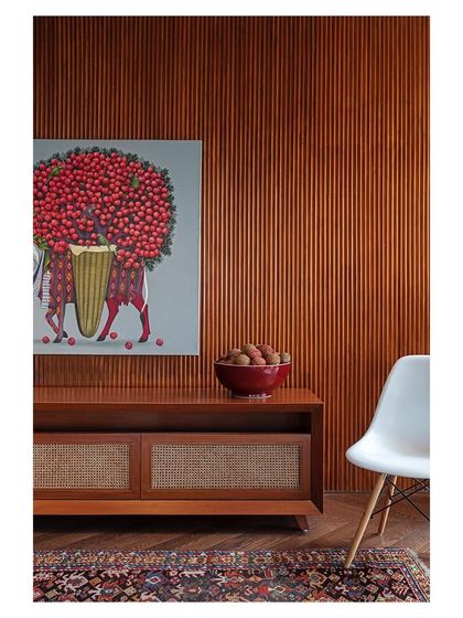 A detail from the Sky Residence project, showcasing a custom-designed console with cane-fronted cabinets. The warm wood tones are set against a fluted wall panel and complemented by vibrant art by L.S. Singh and a 19th-century Kurdish rug.