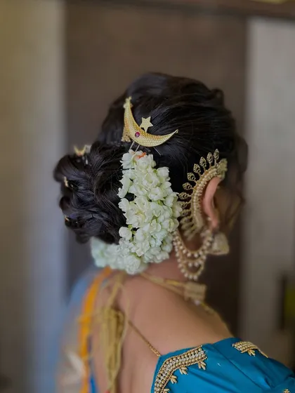 A detailed view of the traditional 'khopa' hairstyle, adorned with fresh jasmine flowers ('gajra') and a 'kainchi' style ear cuff.