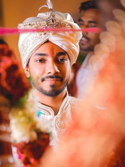 A creative shot of the groom seen through the garlands, capturing his expression during the ceremony.