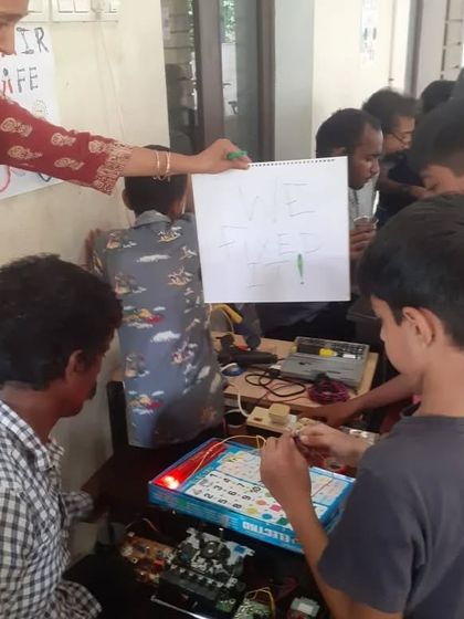 "We fixed it!" A mentor and a group of kids celebrate a successful electronics repair. This moment of shared achievement is what our community is all about.