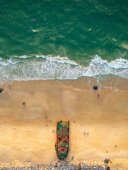 A top-down shot of the shipwreck at Padubidri beach. This abstract view focuses on the textures and colors of the rusted boat against the sand and waves.