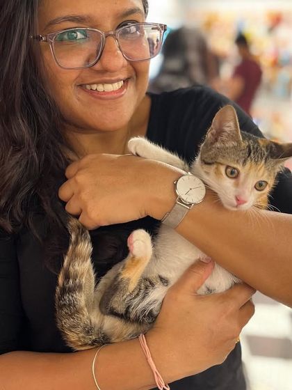 A smiling volunteer holds a calico kitten. The joy on our volunteers' faces reflects the rewarding experience of helping animals find their forever homes.