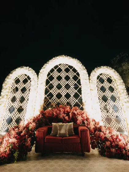 A beautiful photo-op area with a red sofa set against white latticework arches and lush red florals. A perfect spot for guests to capture memories.
