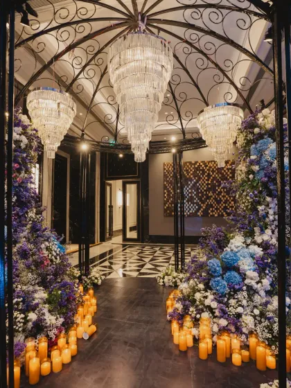The grand entrance to the Sangeet, framed by a wrought-iron dome, cascading chandeliers, and a pathway lined with candles and flowers.
