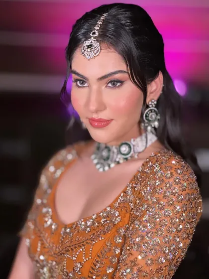 A stunning look in a mustard-colored lehenga. The makeup features a sharp winged liner and a glossy lip, complemented by a beautiful maang tikka.