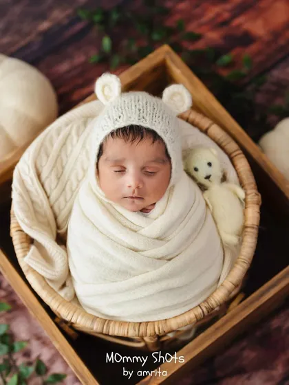 A cozy, neutral-toned setup with a baby in a bear bonnet, nestled in a wooden crate with a teddy bear, showcasing classic prop styling.