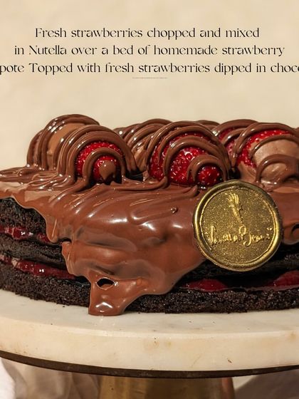 Our Nutella Strawberry cake is back in season. This image shows the rich, glossy Nutella topping and the layers of homemade strawberry compote peeking through.