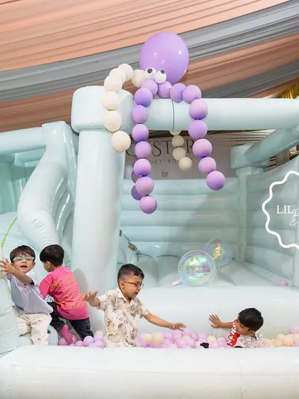 Kids having a blast in the mint green bouncy castle and ball pit at the mermaid-themed party.
