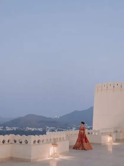A wide-angle shot of the bride standing alone on a palace rooftop at dusk. The soft evening light and the expansive view of Udaipur create a feeling of peaceful solitude and breathtaking beauty.