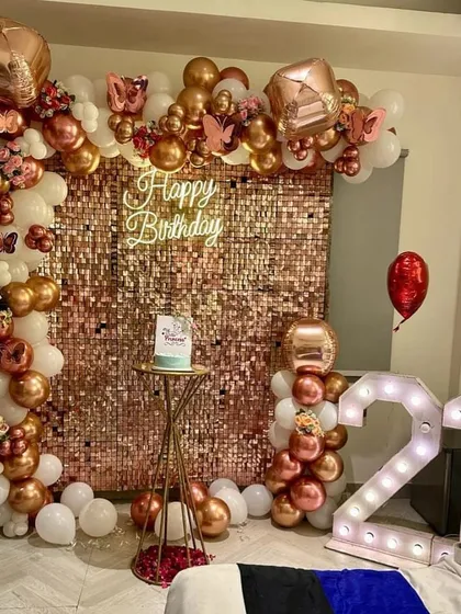 A glamorous 21st birthday setup designed for stunning photos. This decoration features a dazzling rose gold sequin wall, a custom neon sign, and an organic balloon arch in rose gold and white, complemented by large '21' marquee lights.