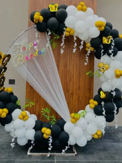 A black, white, and yellow balloon ring with butterfly accents and a draped curtain.