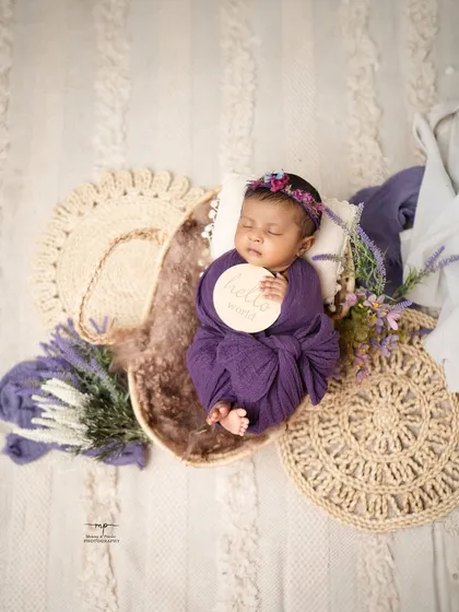 An overhead shot of a newborn swaddled in purple, holding a "hello world" sign. This classic newborn pose is a wonderful way to announce your new arrival.