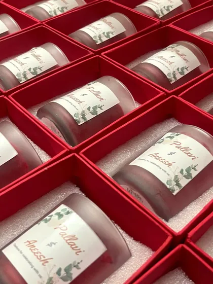A beautiful bulk order of custom wedding favors. These frosted red jar candles feature personalized labels for the couple, packed neatly in custom red boxes, ready for the celebration.