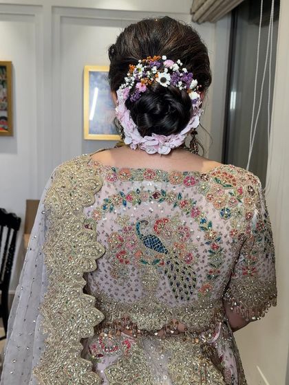 A delicate bridal bun decorated with a mix of colorful, small flowers. This style is perfect for a bride wearing a pastel lehenga with multi-colored embroidery, like the peacock design seen here.