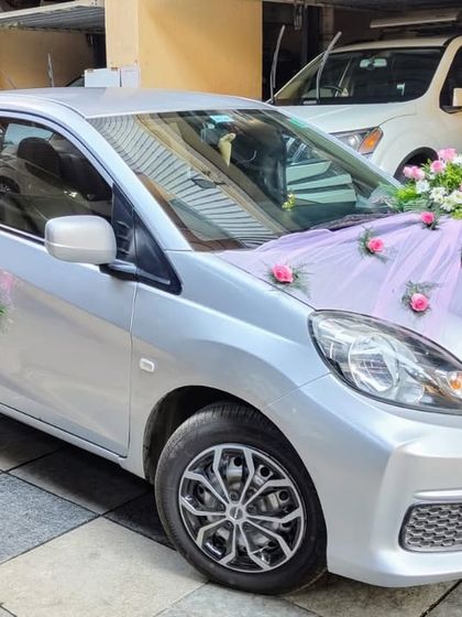 A delicate and pretty decoration for a silver Honda Amaze. A light purple net is draped over the bonnet, dotted with pink roses, while small bouquets adorn the side mirrors.