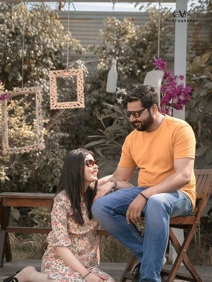 A lovely, sunlit pre-wedding portrait of a couple in a garden setting, capturing their happy and relaxed interaction.