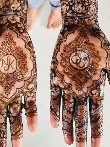 The engagement mehendi for Kavitha, featuring her and her partner's initials 'NK' on one palm and a symbol of interlocking rings on the other.