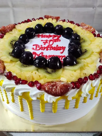 A fresh fruit cake celebrating a 70th birthday. This healthy and delicious option is topped with seasonal fruits like pineapple, kiwi, pomegranate, figs, and cherries.