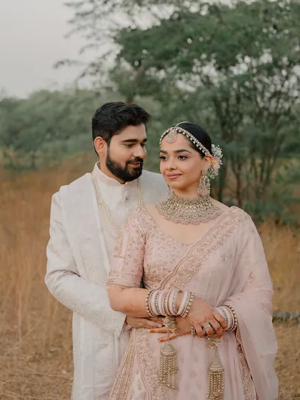 A romantic outdoor portrait. The bride's blush pink lehenga and soft makeup blend beautifully with the natural surroundings.