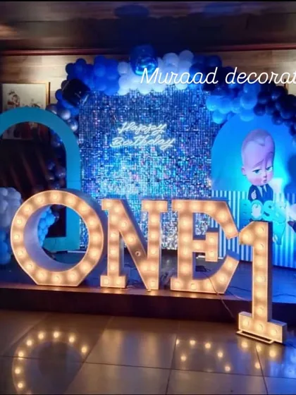 This Boss Baby theme is perfect for a little one turning one. The setup features a blue sequin wall, character cutouts, and large, illuminated 'ONE' letters, creating a fun and impressive stage for the celebration.