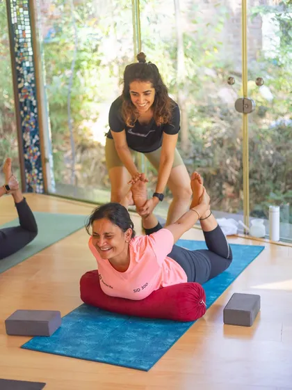 A joyful moment assisting a student in a supported backbend using a bolster. Props help us access poses with more ease and find a deeper release.