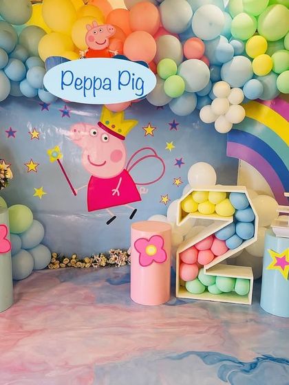 A playful Peppa Pig theme with a rainbow and clouds backdrop. The decor includes a custom Peppa cutout, pastel-colored plinths, and a balloon-filled marquee number '2'.