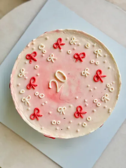 A top-down view of this delicate 20th birthday cake, showing the soft blush watercolor effect on the buttercream, surrounded by tiny hand-piped red and white bows.