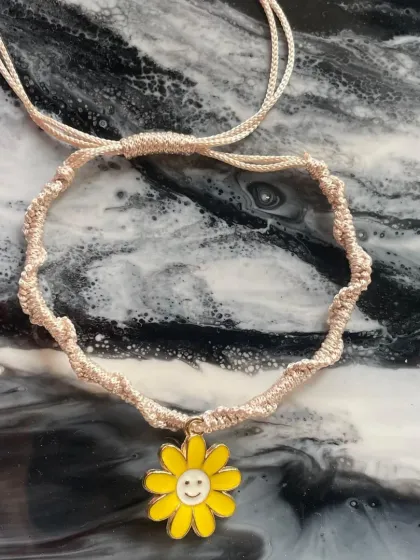 A cheerful macrame bracelet with a smiling sunflower charm. This piece is designed to bring a little bit of sunshine and happiness to your day.