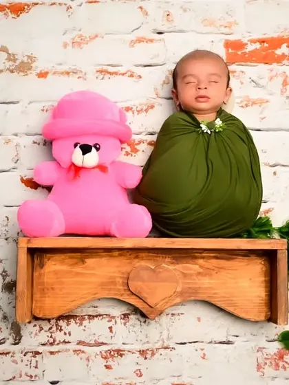 A sweet newborn portrait with a teddy bear companion. The simple setup on a wooden shelf against a brick wall adds a rustic charm.