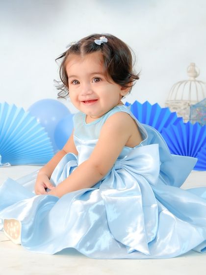 A beautiful baby girl in a satin blue dress, celebrating her milestone. The blue paper fans and decorations create a simple yet elegant birthday setup.