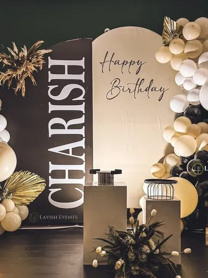 A modern take on the boho theme. This setup for a 3rd birthday combines a personalized black and white backdrop with pampas grass, dried palms, and a neon number.
