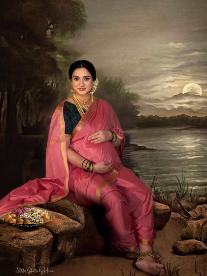 A full-length portrait of a mother-to-be in a pink saree, set against a painted moonlit backdrop. This artistic photo captures a serene and beautiful moment inspired by classic paintings.