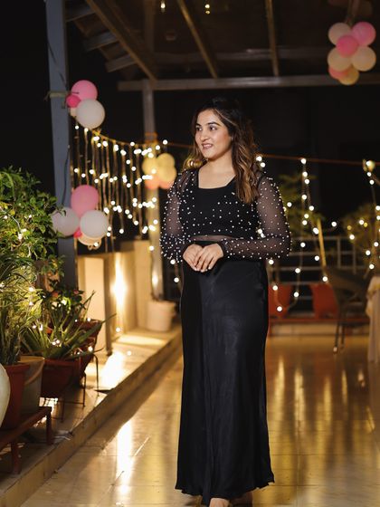 Another shot of the all-black look. The pearl-studded sheer top adds a touch of modern glamour, while the satin skirt keeps it elegant and timeless.