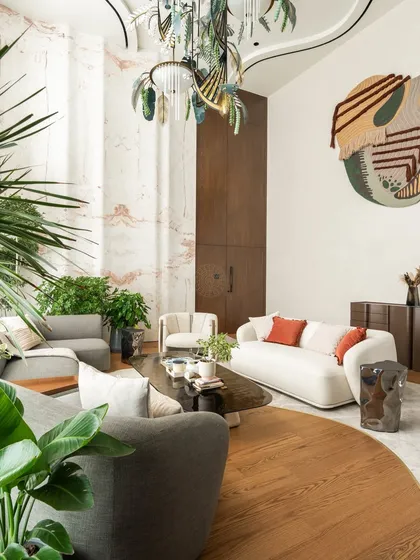 This is the double-height living room in a 5000 sq ft Kolkata home that became one of our most talked-about projects. The centerpiece is a 22-foot-tall, hand-crafted marble wall that took over five months to complete. We designed the space with flowing curves, mixing wood and marble flooring to create a sense of fluidity that connects the living, dining, and kitchen areas.