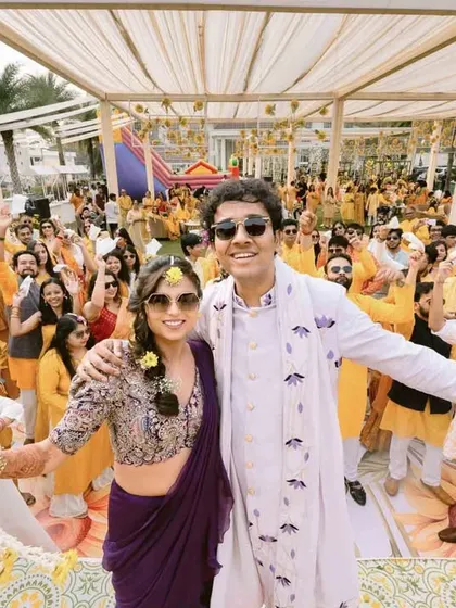 The couple and their friends celebrate with abandon at their Haldi ceremony, a wide shot capturing the energy of the crowd.