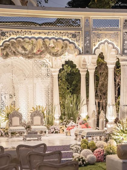 The wedding mandap, a masterpiece of white-on-white elegance. Intricate jali work, Mughal-style arches, and delicate floral garlands create a sacred space that is both grand and deeply personal.