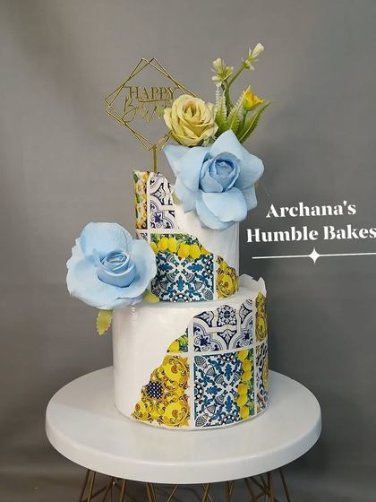 A unique two-tiered cake with a mosaic tile pattern and large blue sugar flowers. A piece of edible art.